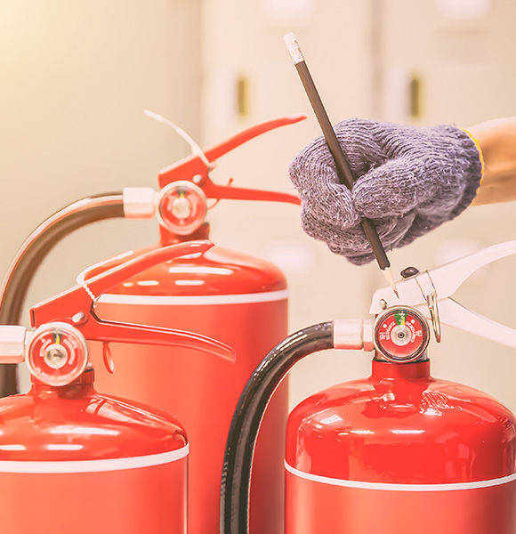 hand holding a pencil next to red fire extinguishers highlighting the importance of fire safety training tips and 7 methods for effective fire prevention