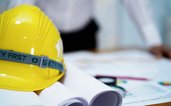 yellow safety helmet on blueprints with person in background ensuring workplace safety and health in nine construction areas