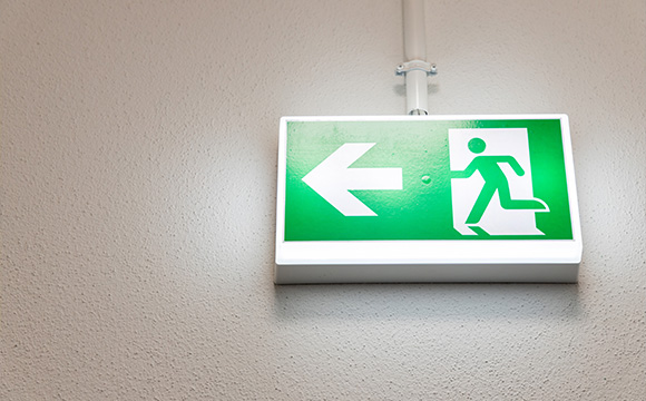 green emergency exit sign pointing left with a figure running towards a door indicating safe escape route number 13