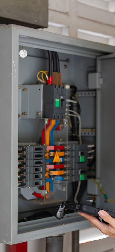 electrical control panel with colorful wires and circuit breakers showing hand holding device for testing seven electrical connections